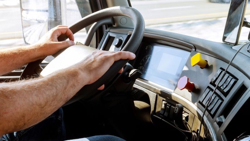 Foto horizontal colorida mostra mãos masculinas em um volante com painel de caminhão