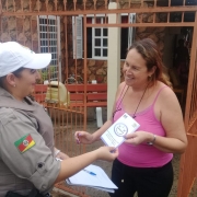 Policial militar feminina entrega para outra mulher folder com informações das Patrulhas Maria da Penha durante a 3ª Operação Integrada Metropolitana