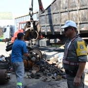 Garra mecânica recolhe peças de ferro-velho vistoriado em Parobé. Em primeiro plano, policial militar observa o trabalho de homens que colocam peças em pilha de recolhimento.