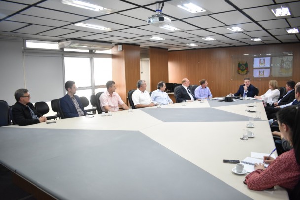Grande mesa de reunião, rodeada por prefeitos do Alto Uruguai em encontro com Ranolfo Vieira Júnior, sentado à ponta da mesa, ao fundo da imagem.