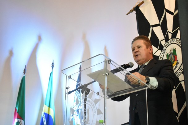 Ranolfo Vieira Júnior discura em púlpito no auditório da Polícia Civil. Ao fundo, brasão da corporação e bandeiras.