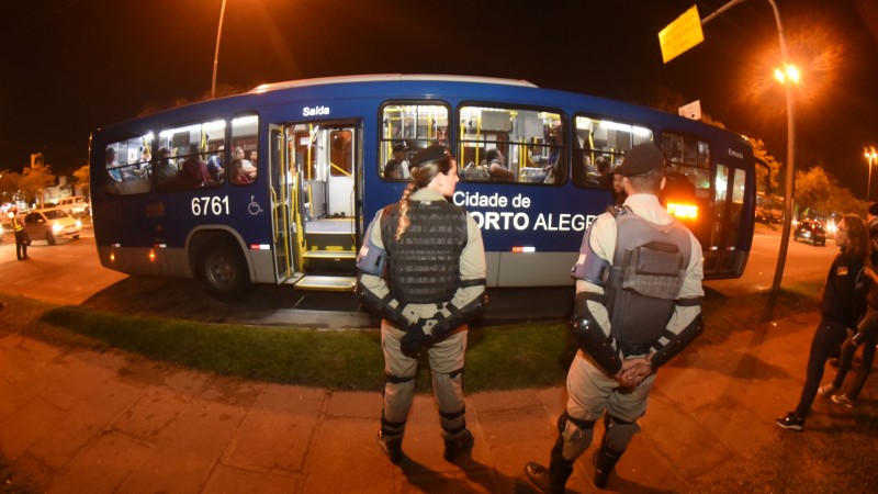 Dois policiais militares observam ônibus de linha da Capital.