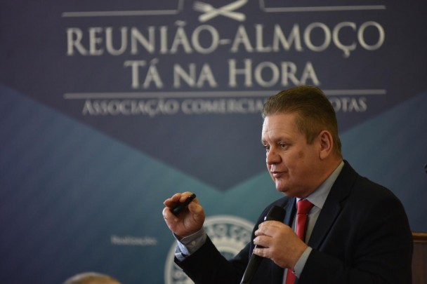 Ranolfo Vieira Júnior fala ao microfone. Ao fundo, banner da reunião-almoço Tá na Hora, da Associação Comercial de Pelotas.