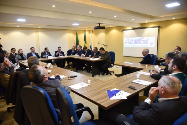 Vice-governador e prefeitos da região Sul do RS durante reunião na sede da associação. Ao fundo, telão com a logomarca da AZONASUL.
