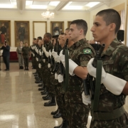Fileira de homens da Polícia do Exército seguram fuzis transferidos para a Brigada Militar em salão do Comando Militar do Sul.