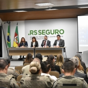 Palestra no auditório da SSP. Quatro autoridades na mesa da cerimônia à frente da platéia. Ao fundo, marca do RS Seguro.