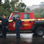 Dois bombeiros em posição de continência ao lado de uma caminhoneta da corporação.