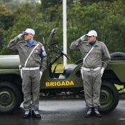 Dois policiais militares em posição de continência ao lado de um jipe da corporação