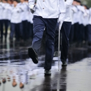 Militar com espada em punho é mostrado apenas da cintura para baixo, marchando em avenida durante o Desfile de 7 de setembro em Porto Alegre. Ao fundo, restante da tropa.