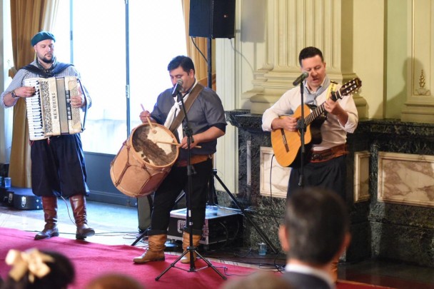 Três músicos, um com uma gaita, outro com um bumbo leguero e o terceiro com violão, executam música durante celebração do aniversário no IGP, no salão Negrinho do Pastoreio, no Piratini.