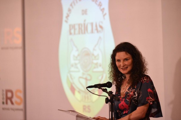 Heloísa Kuser, diretora do IGP, discursa em frente a um microfone. Ao fundo, telão com projeção do logo do IGP.