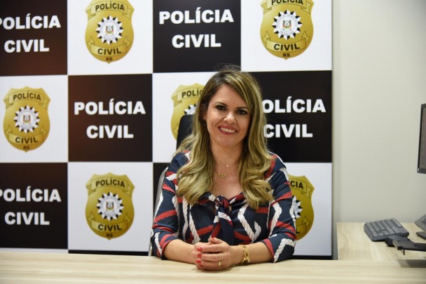 Raquel Paim da Silva Schneider, titular da 1ª DPPA de Santa Cruz do Sul, aparece sentada em frente a um banner com o brasões da Polícia Civil e o nome da instituição.