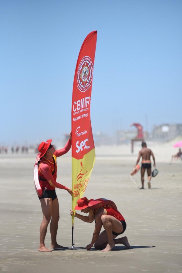 Dois guarda-vidas ficam uma bandeira de sinalização na areia da praia de Tramandaí.