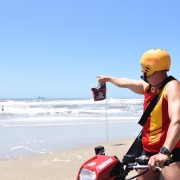 Guarda-vida em um quadriciclo na areia da praia de Tramandaí aponta com o braço estendido na direção do mar.