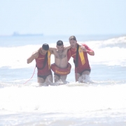 Dos guarda-vidas carregam banhistas para fora do mar durante simulação de resgate na praia de Tramandaí.