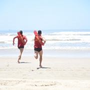 Dois guarda-vidas equipados com life-belt correm em direção ao mar na praia de Tramandaí.