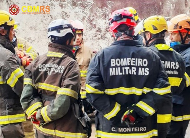 Foto mostra bombeiros militares reunidos em uma roda de conversa. Em destaque, dos servidores de costas vestindo uniforme as inscrições "Bombeiros Militar MS" e "Bombeiros Minas Gerais".