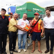 Comandante do CBMRS, representante da Unimed, vice-governador, guarda-vidas uniformizado, governador e bombeiros militar uniformizado aparecem lado a lado. Representante da Unimed, vice-governador e guarda-vidas seguram um desfibrilador doação pela empres