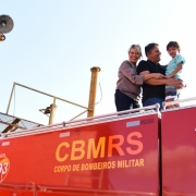 Mãe, pai e filho, no braços do homem, estão em cima de um caminhão do CBMRS. Na lateral do veículo, está escrito o nome da corporação.