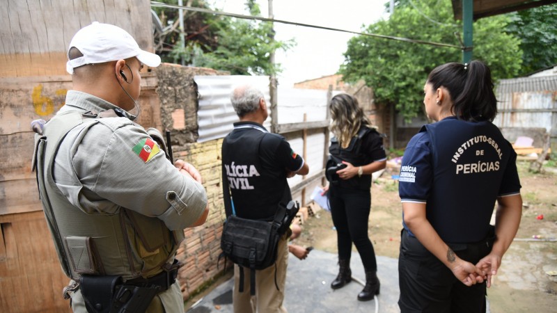 Em um pátio de uma casa, um policial militar, dois policiais civis (um homem e uma mulher) e um servidora do IGP.
