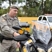 Comandante-geral da BM, coronel Rodrigo Mohr, segura o guidom de uma motocicleta entregue ao CRBM. Ao fundo, duas caminhonetes. 