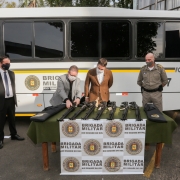 Em frente a um micro-ônibus, vice-governador Ranolfo e governador Eduardo Leite, observam armas sobre uma mesa com banner da Brigada Militar. À esquerda, o secretário adjunto cel. Marcelo Gomes Frota. À direita, o comandante-geral da BM, cel Rodrigo Mohr.
