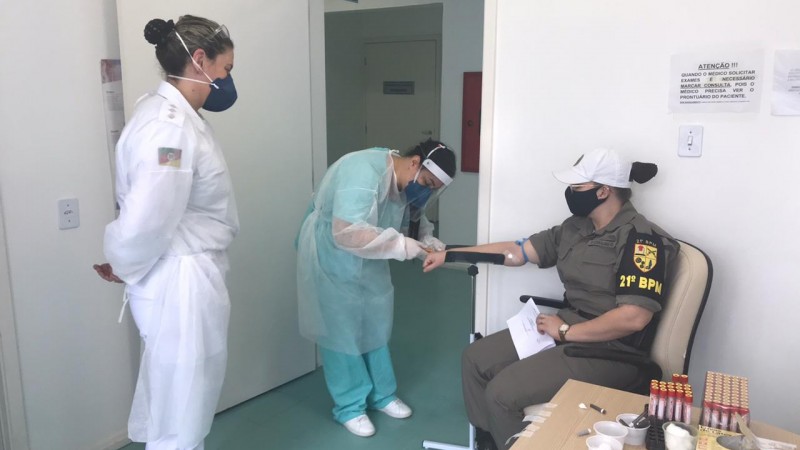 Duas profissionais da saúde aplicam o teste de sangue em uma policial militar. 