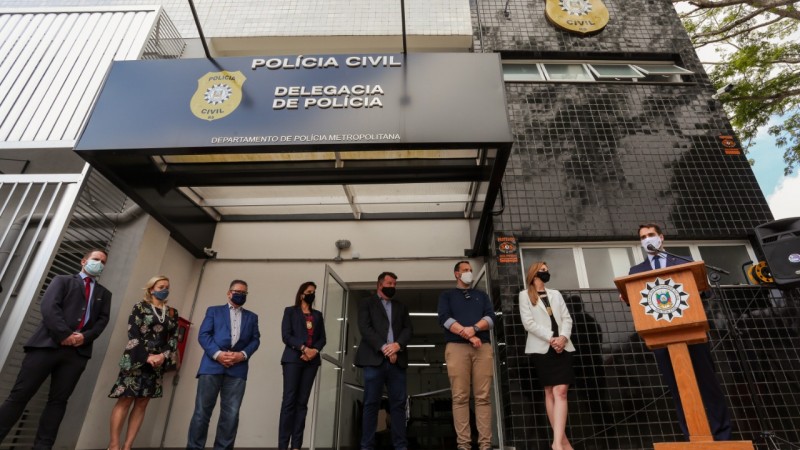 Em frente ao novo prédio da Delegacia de Polícia de Guaíba, governador está à direita da imagem, discursando ao microfone diante de um púlpito. À esquerda, outras autoridades observam.