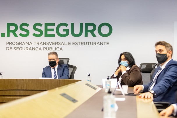 em frente a um grande painel escrito "RS SEGURO" o vice-governador Ranolfo Vieira Júnior, a ministra da Mulher, da Família e dos Direitos Humanos, Damares Alves, e o deputado estadual, tenente-coronel Zucco, estão sentados em uma mesa de reuniões
