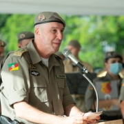 Comandante-geral da Brigada Militar, coronel Rodrigo Mohr Picon, enunciando nova sede e homenageando colaboradores em um microfone. Atrás dele, membros da academia militar em desfoque.