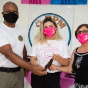 Um agente da Brigada e duas mulheres estão segurando juntos uma mesma mecha de cabelo para simbolizar a doação de cabelos para o Imama e o Instituto do Câncer Infantil.