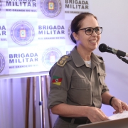Chefe do Estado-Maior Cel Cristine Rasbold fazendo seu discurso de despedida, em frente a um banner da brigada militar.