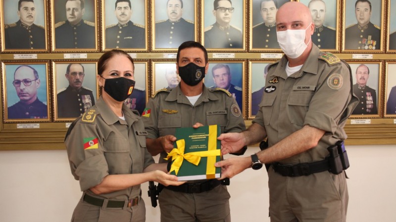 Coronel Cristine ao lado de dois oficiais recebendo suas honrarias no dia de sua despedida. Foto em frente a galeria de oficiais da reserva