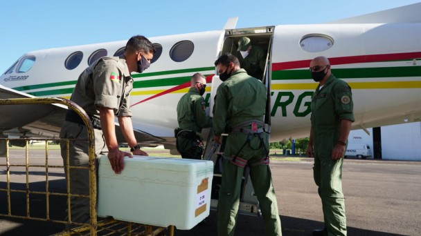 Brigadianos embarcam uma caixa de vacinas em avião bimotor da BM.