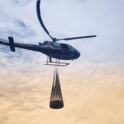 Um helicóptero sobrevoando com uma carga acomplada na parte de baixo da aeronave.