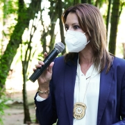 A Chefe da Polícia, Nadine Anflor, discursando segurando um microfone na mão direita. Nadine utiliza uma máscara do tipo PFF2.