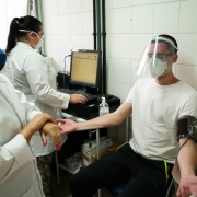Aluno soldado bombeiros de máscara, face shield, camiseta branca e calça preta, realiza doação de sangue.
