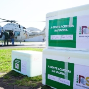 Caixas com os imunizantes empilhadas no chão do aeroporto da BM. Helicóptero ao fundo.