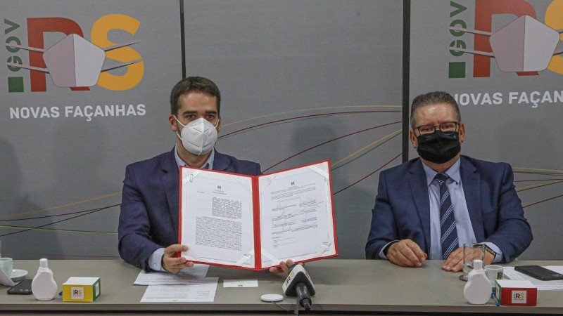 O governador, Eduardo Leite, e o vice-governador e secretário da Segurança Pública, delegado Ranolfo Vieria Júnior, estão sentados, ambos de máscara de proteção, enquanto o governador segura o documento impresso do acordo. 