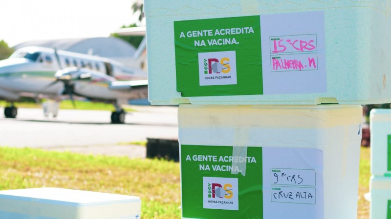 Duas caixas térmicas empilhadas no aeroporto da Brigada Militar, um avião atrás, em desfoque, esperando para ser carregado.