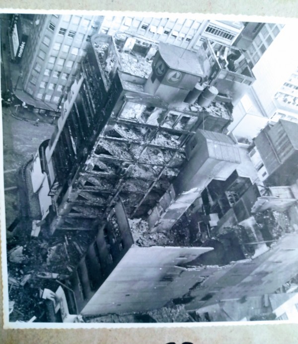 Foto tirada de dentro um prédio mostrando a loja que incendiou. A foto foi tirada na diagonal, de um ângulo acima da estrutura incendiada, mostrando as paredes expostas e os diversos andares incinerados.