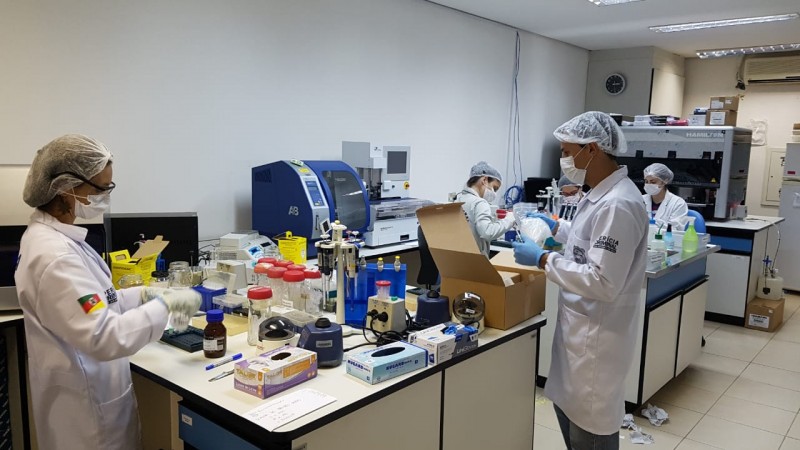 Quatro servidores com jaleco e EPIs de laboratório, fazendo análises de amostras