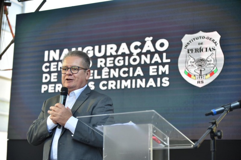 Vice-governador e secretário da SSP, delegado Ranolfo Vieira Júnior, em pé, de camisa branca e terno cinza, segurando um microfone, fala durante a inauguração do Crepec. Atrás, telão azul com o texto "Inauguração Centro Regional de Excelência em Perícias Criminais", ao lado do logo do IGP.