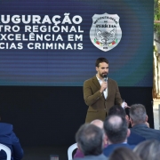 Governador Eduardo Leite, em pé, de camisa branca e terno marrom, segurando um microfone, fala durante a inauguração do Crepec diante de um plateia sentada. Ao fundo, telão com logo do IGP e texto "Inauguração Centro Regional de Excelência em Perícias Criminais".