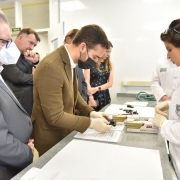 Governador e vice-governador conheceram instalações e tecnologias no prédio inaugurado do Crepec-Sul. O governador, em pé, de terno marrom e vestindo luvas cirúrgicas, segura um objeto sobre uma bancada, diante da qual, do outro lado, está uma perita do IGP. Ao lado, Ranolfo, em pé, de terno cinza, observa.