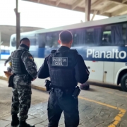 PM e Policial Civil em pé lado a lado em uma plataforma da rodoviária de porto alegre diante de um ônibus da empresa Planalto.