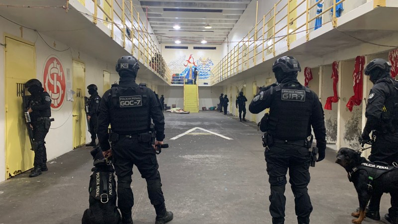 Foto mostra policiais e cão da Polícia Penal de costas em um corredor de cadeia.