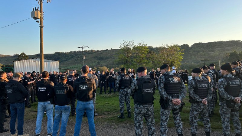 Foto em espaço aberto mostra policiais civis e militares reunidos em círculo. Ao fundo, se vê mata em morro.