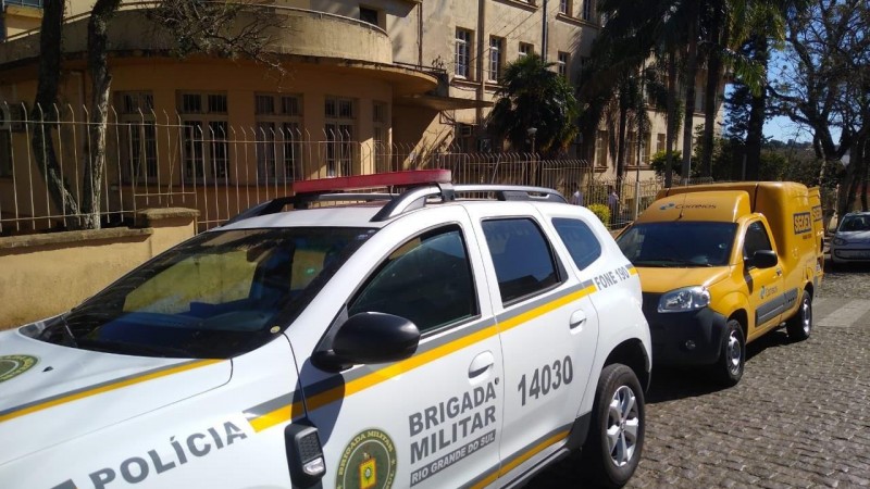 viatura da Brigada Militar e carro dos Correios em frente a instituição de ensino