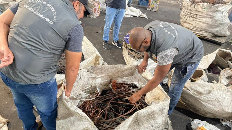 Foto mostra dois homens com colete da SSP manuseando saco cheio de fios.